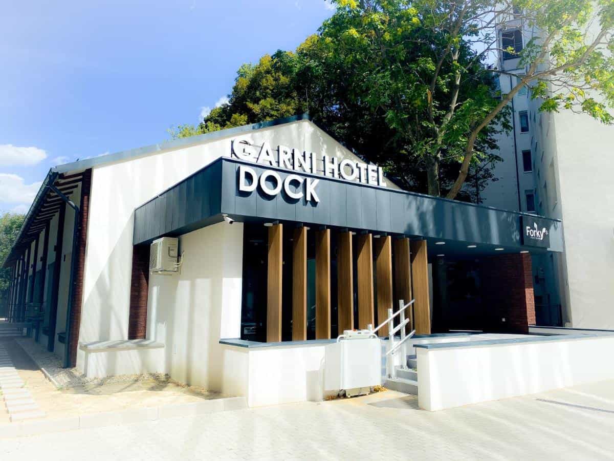 Garni Hotel DOCK entrance with white facade and large green trees overhead in Bratislava