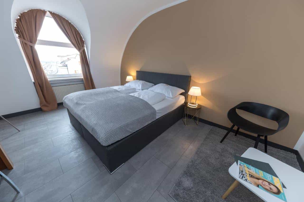 Hotel Atrigon room with a double bed, arched window with brown curtains, and modern furniture.