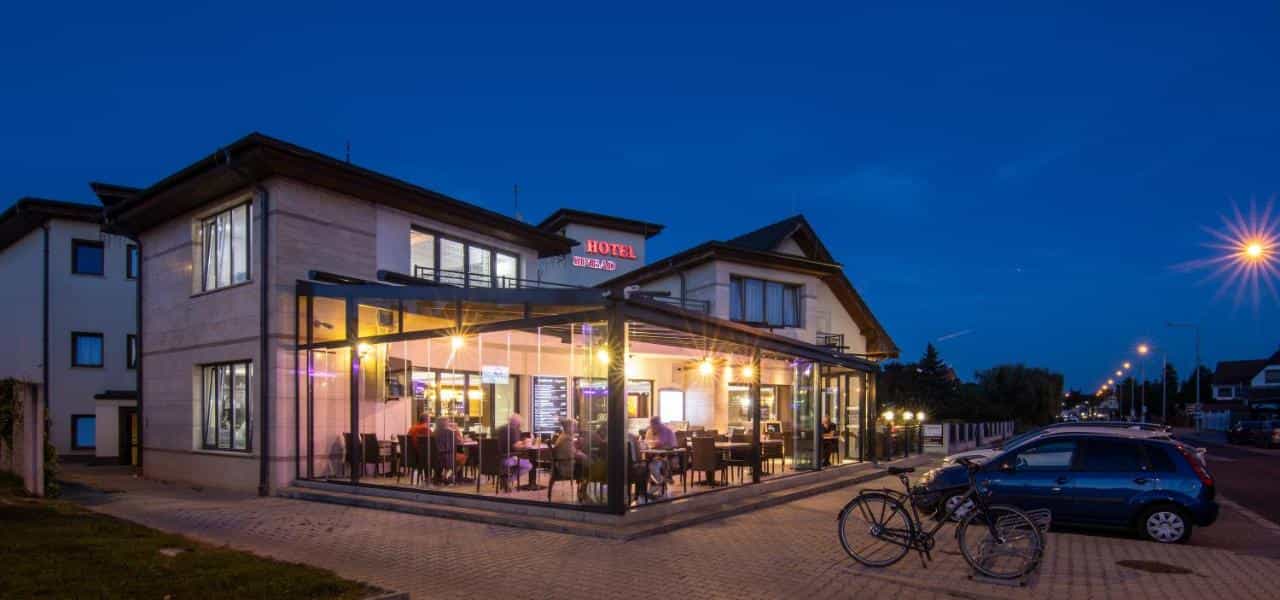 Hotel Simbad exterior with illuminated glass dining area at dusk, bicycles parked nearby.