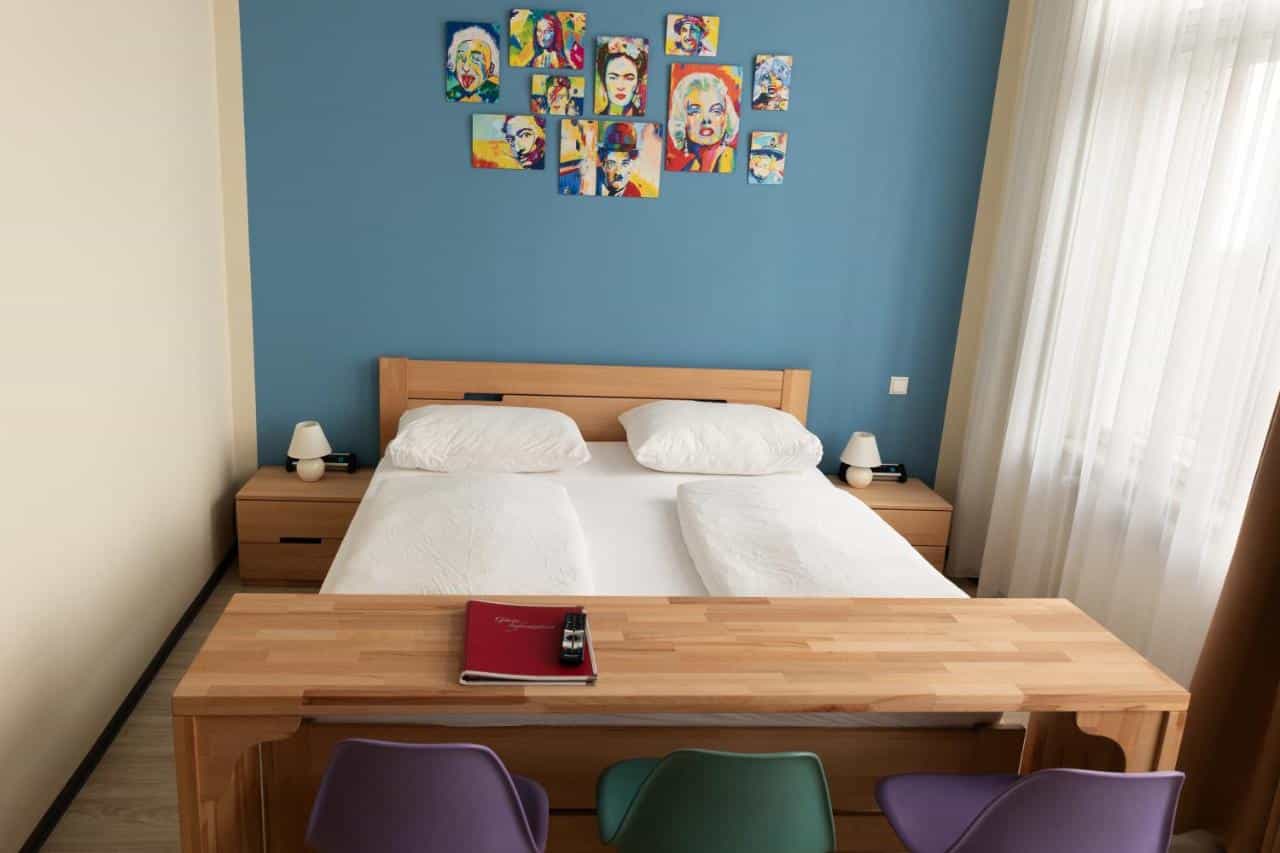 Bedroom with wooden furniture, white bedding, blue accent wall, and pop art portraits.