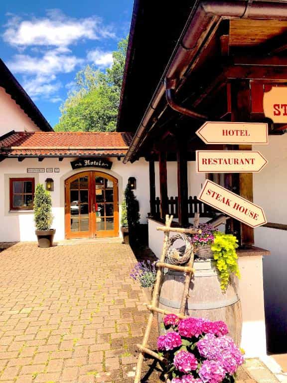Hotel entrance with wooden signs, cobblestone courtyard, and decorative barrel with flowers.