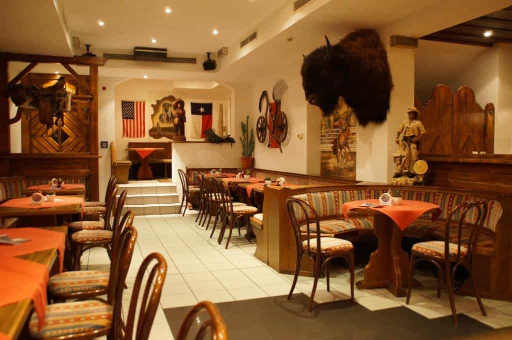 Western-themed restaurant interior with wooden furniture, bison head mount, and American flags on the wall.