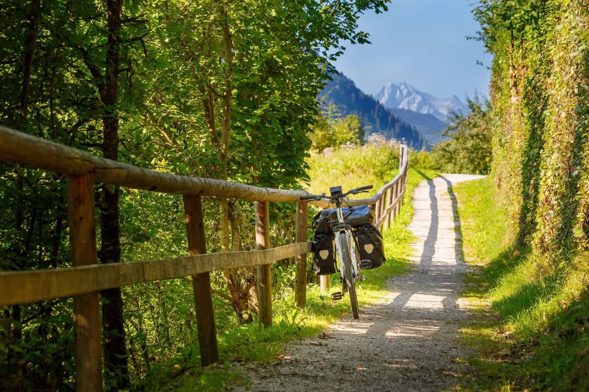 Bikepacking on gravel path with wooden fence, mountains in background, Austria.