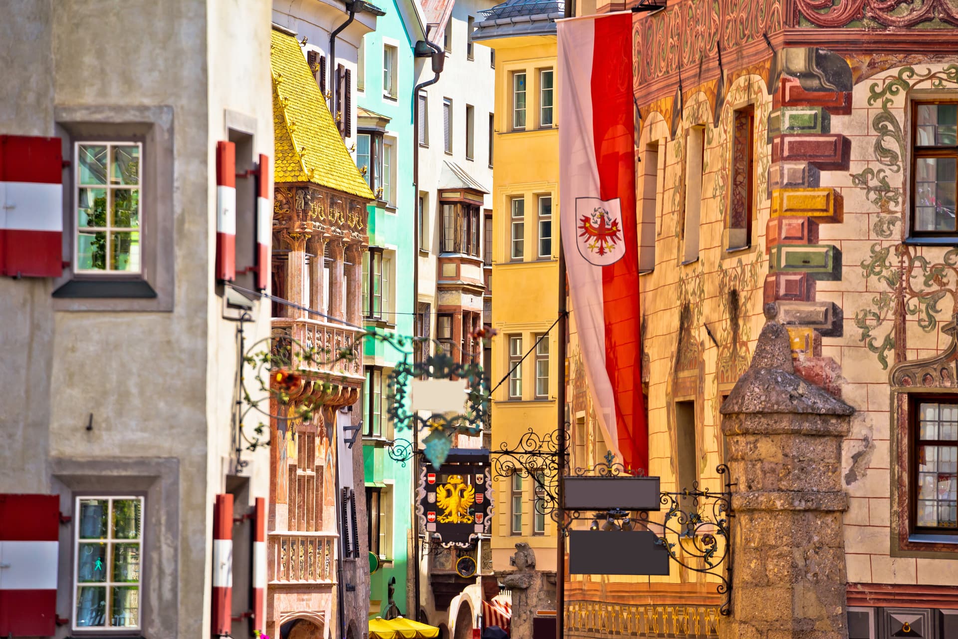 Historic street in Innsbruck with colorful buildings, painted facades, and an Austrian flag.