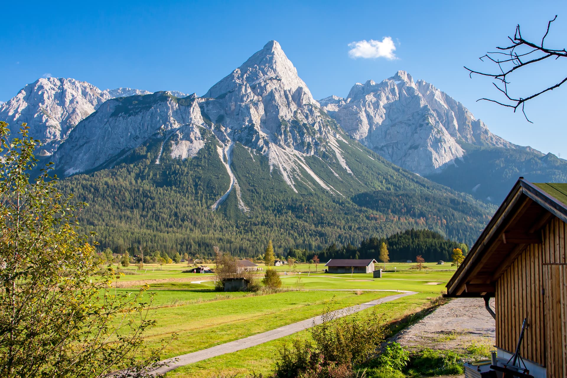 Alpine landscape near Pfunds, Austria, with rocky mountains, green fields, and a wooden building.