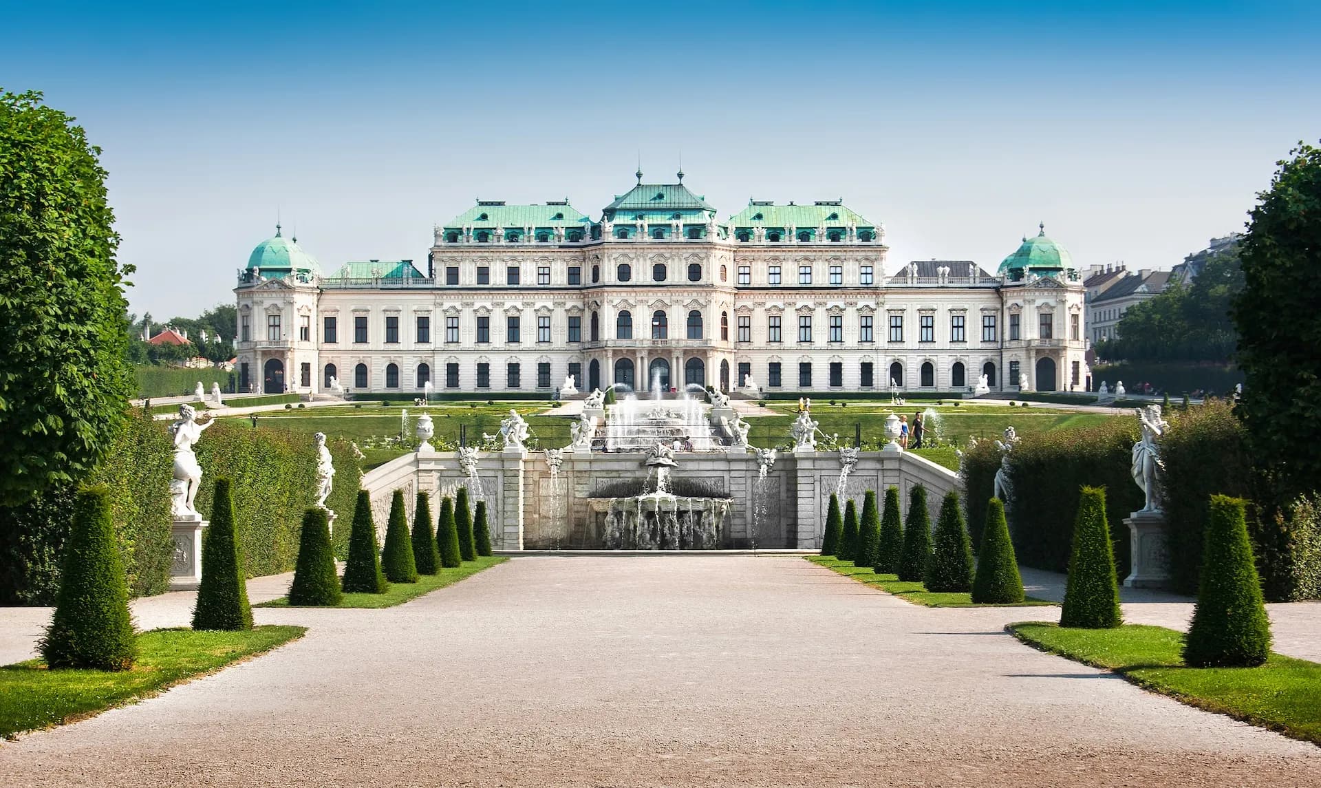 Baroque palace in Vienna with tiered fountain, statues, and manicured gardens under blue sky.