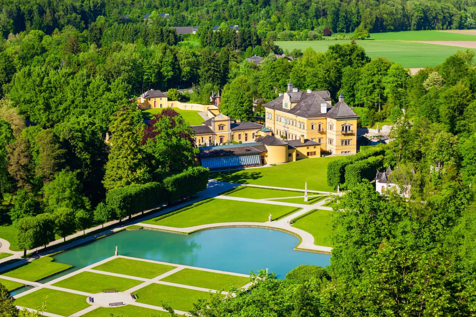Baroque palace with yellow facade surrounded by lush green gardens and reflecting pool in summer.