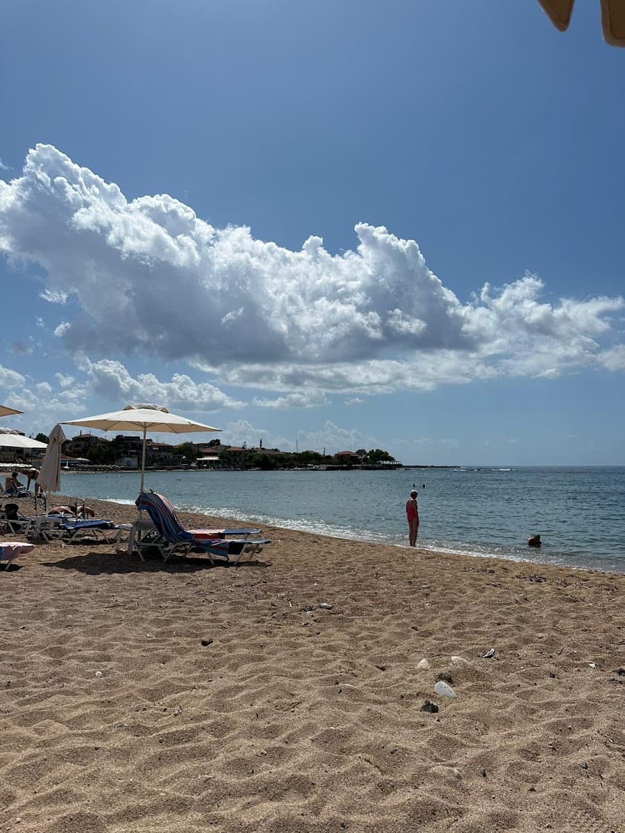Sandy beach with lounge chairs under umbrellas and people wading in calm coastal water