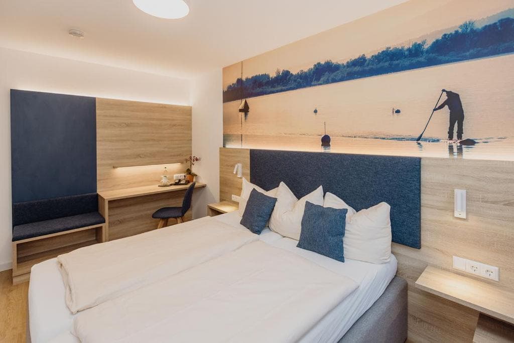 Modern hotel room with double bed, desk, and wall mural of a person paddleboarding on water.