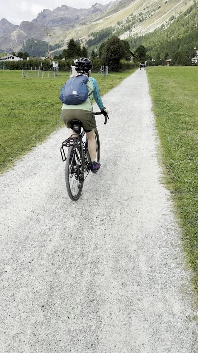 Cyclist riding on gravel path through alpine valley with mountains