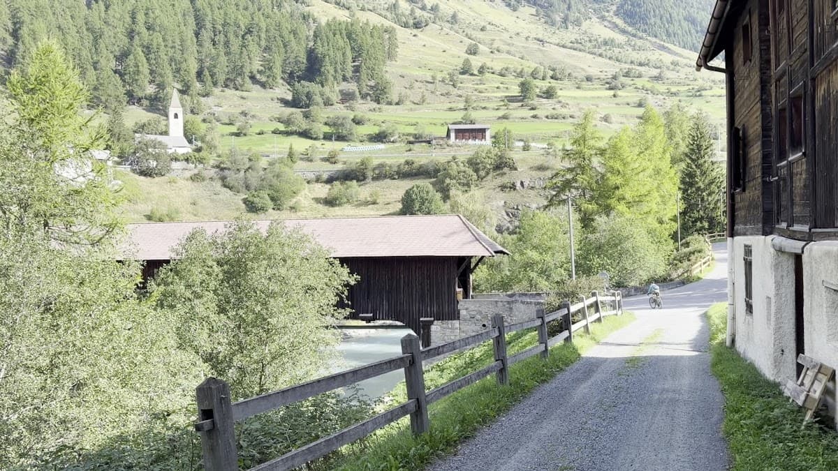 Cyclist on gravel road with wooden bridge, river, and alpine valley view