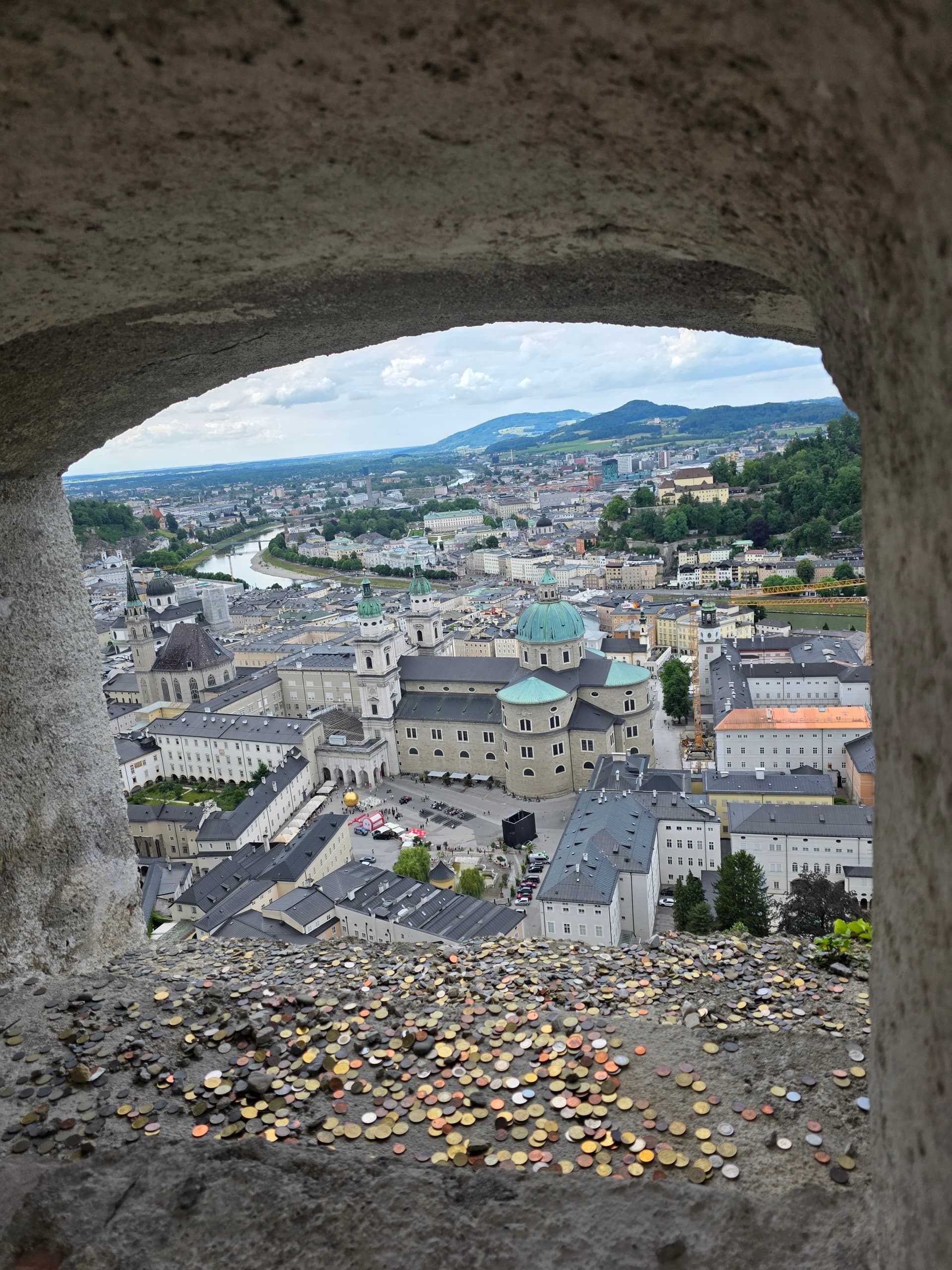 Salzburg rooftops and cathedral viewed through a stone fortress window with coins on the ledge