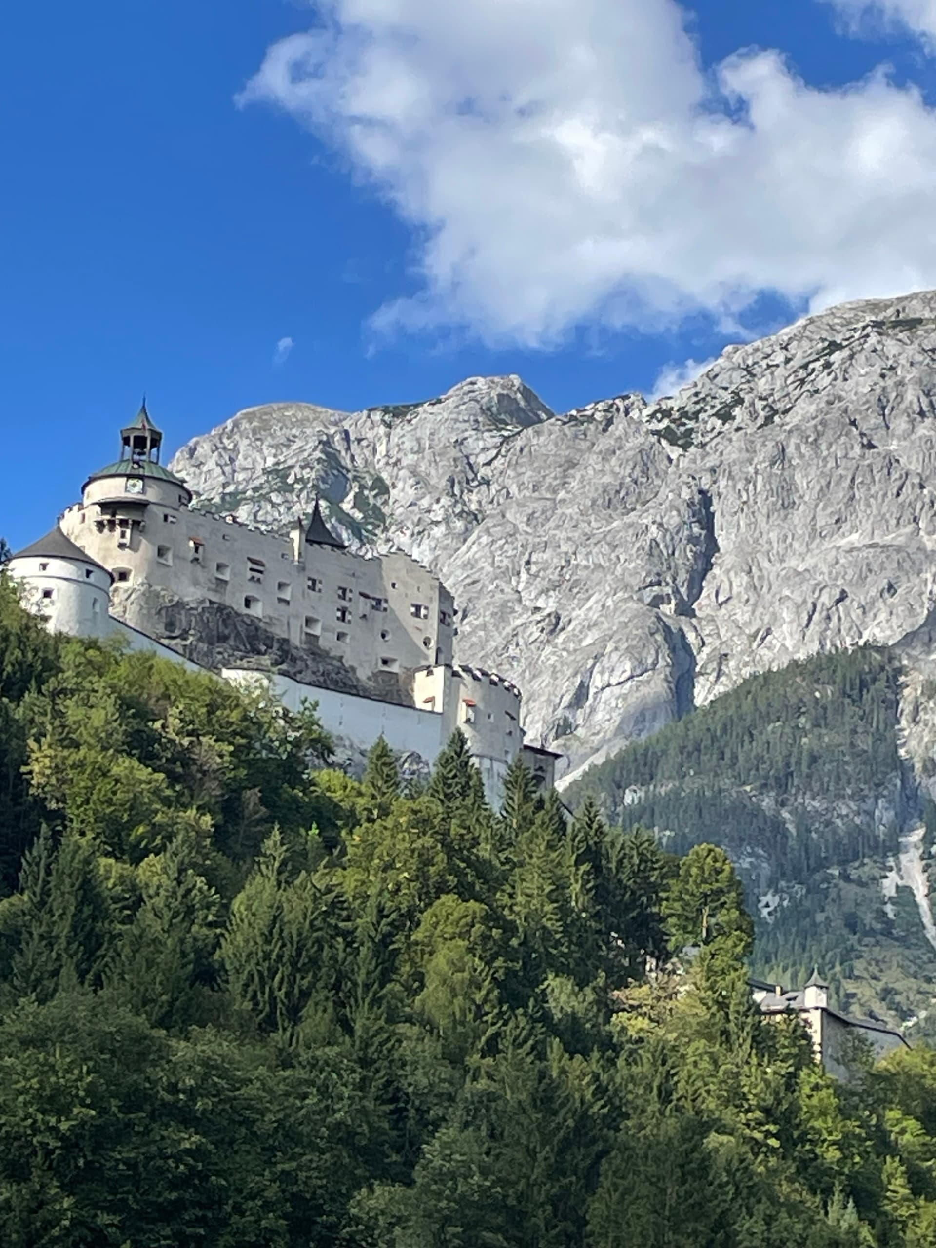 Hohenwerfen Castle on a wooded hillside below towering alpine mountains