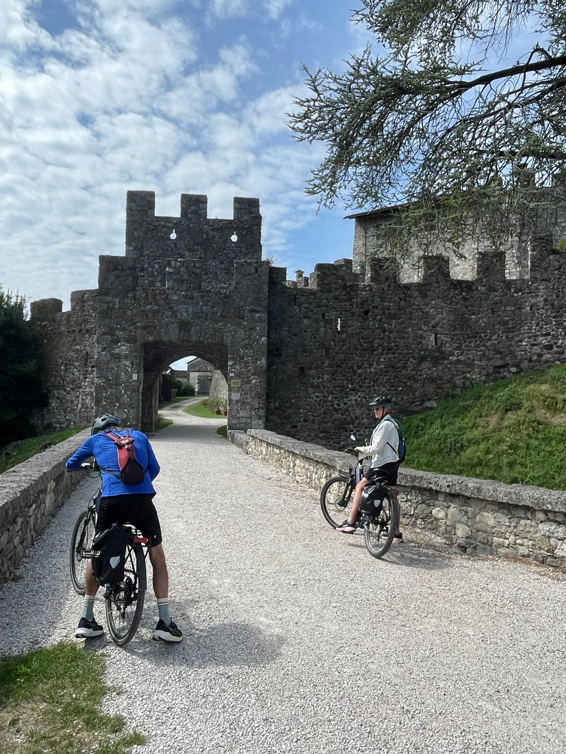 Cyclists with loaded touring bikes approaching a historic castle gate and stone bridge