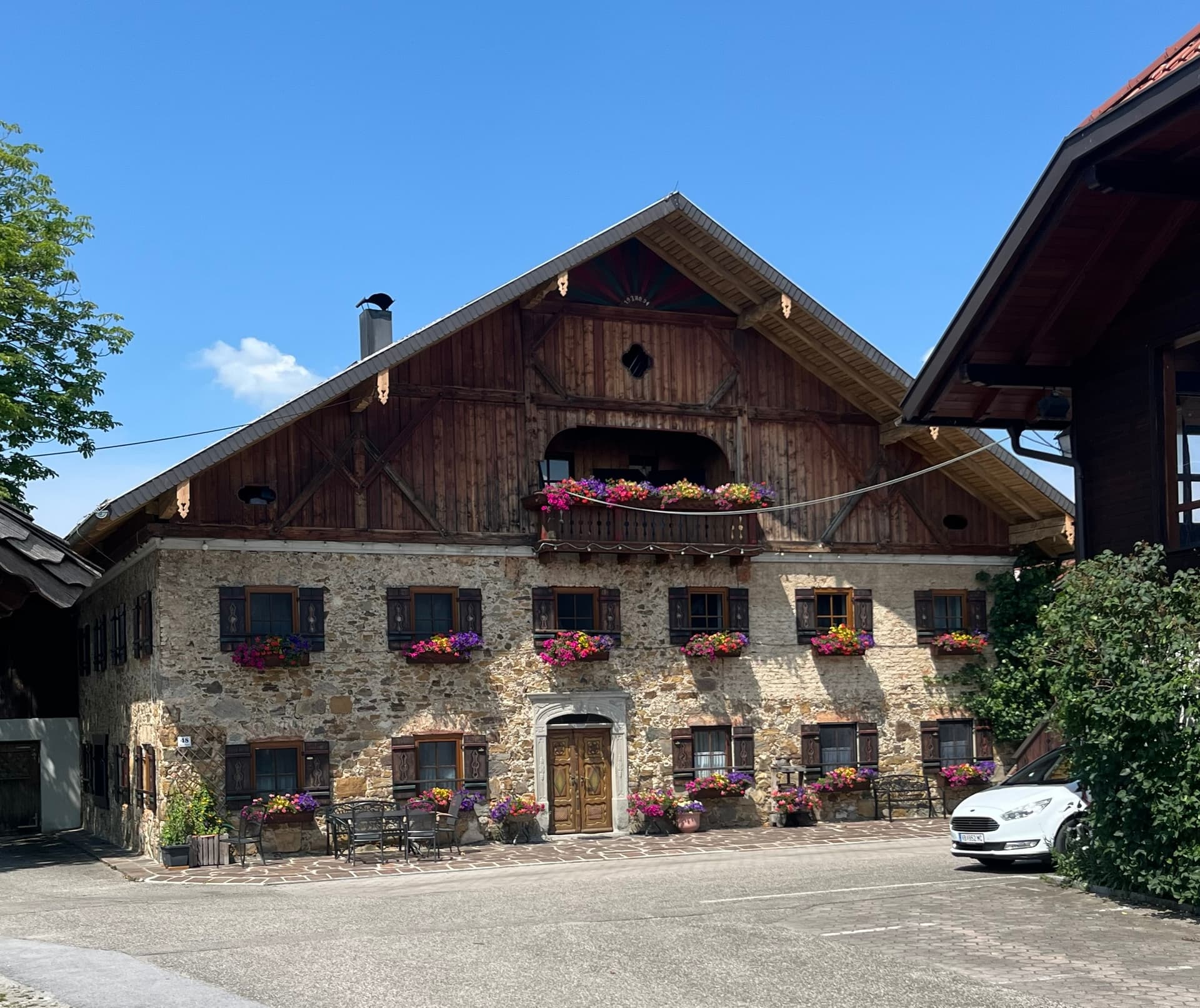 Traditional stone farmhouse with wooden upper floor and colorful flower boxes in windows