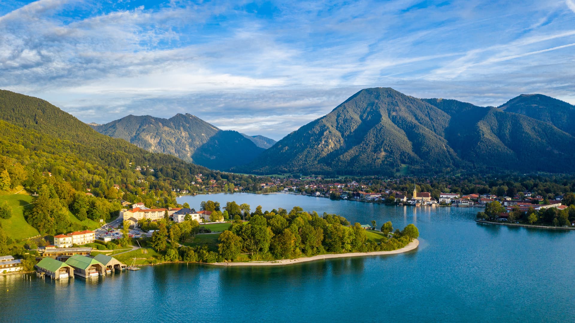 Alpine lake with turquoise water, town, and forested mountains under blue sky at Tegernsee.