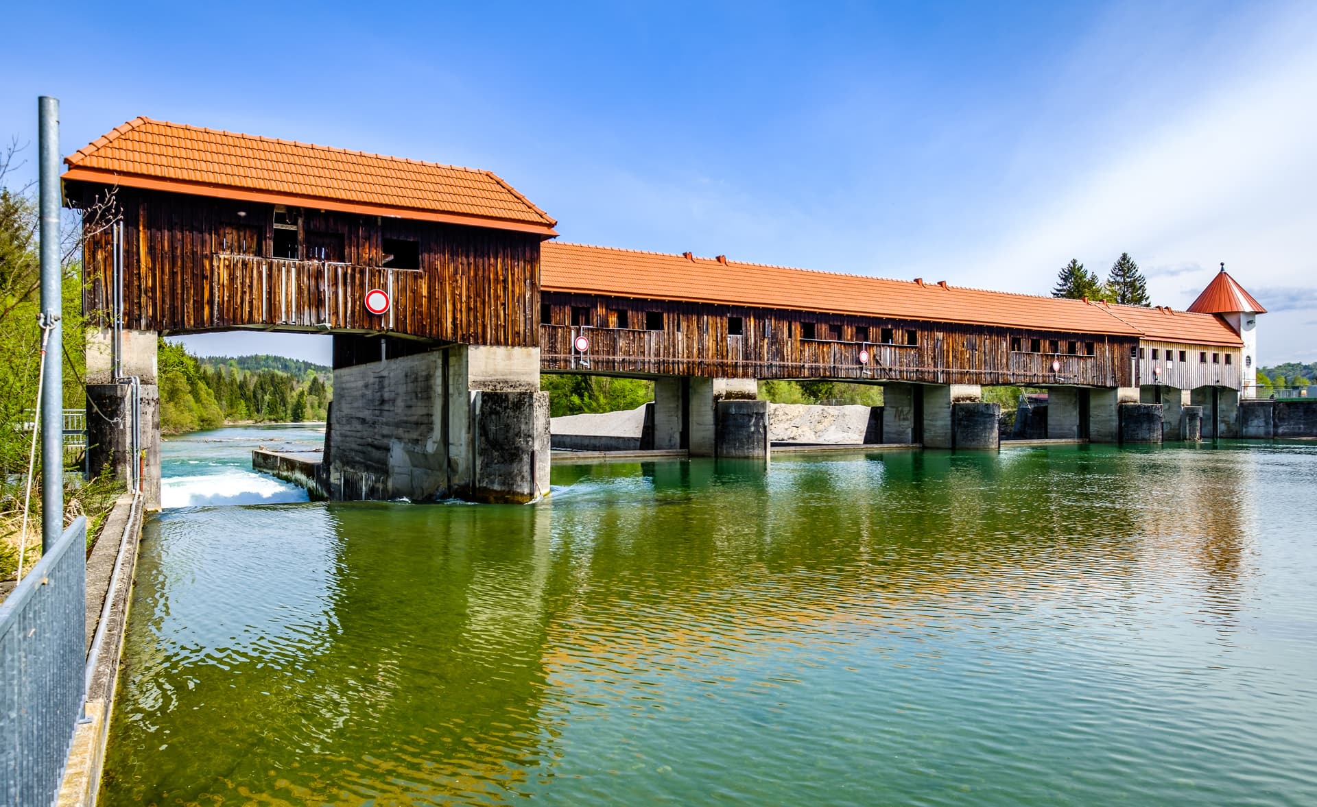 Ickinger Wehr water management structure with wooden building and orange roof over green water.