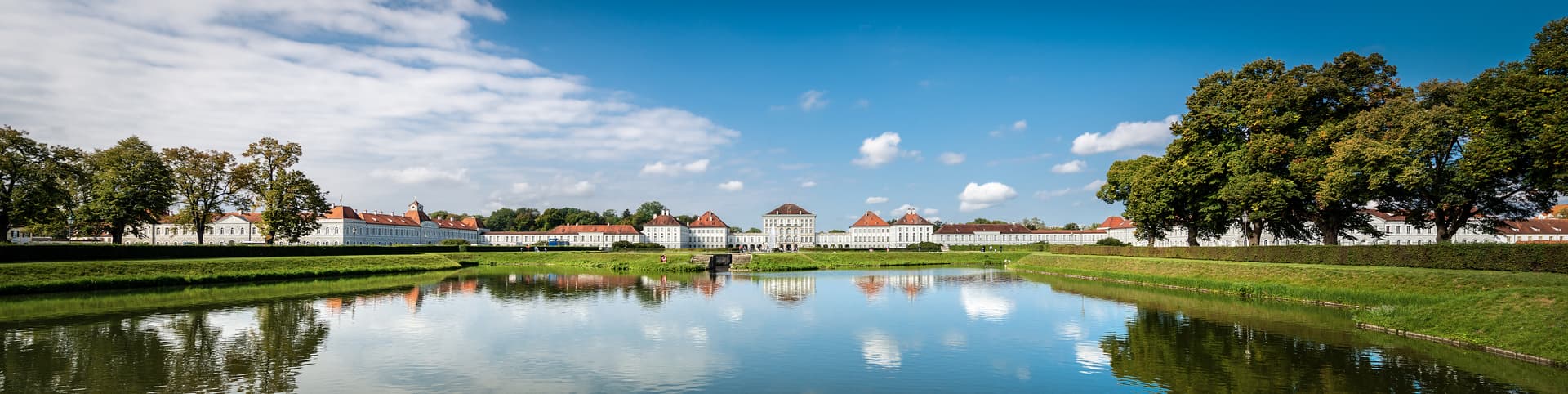 Nymphenburg Palace reflected in the canal under a bright blue sky with white clouds, Munich.