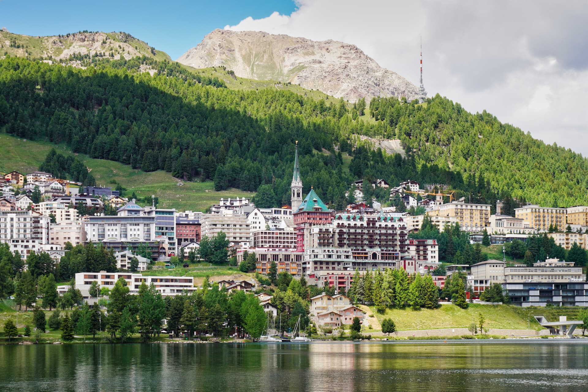 St. Moritz townscape with Lake St. Moritz, green slopes, and rocky alpine mountains.