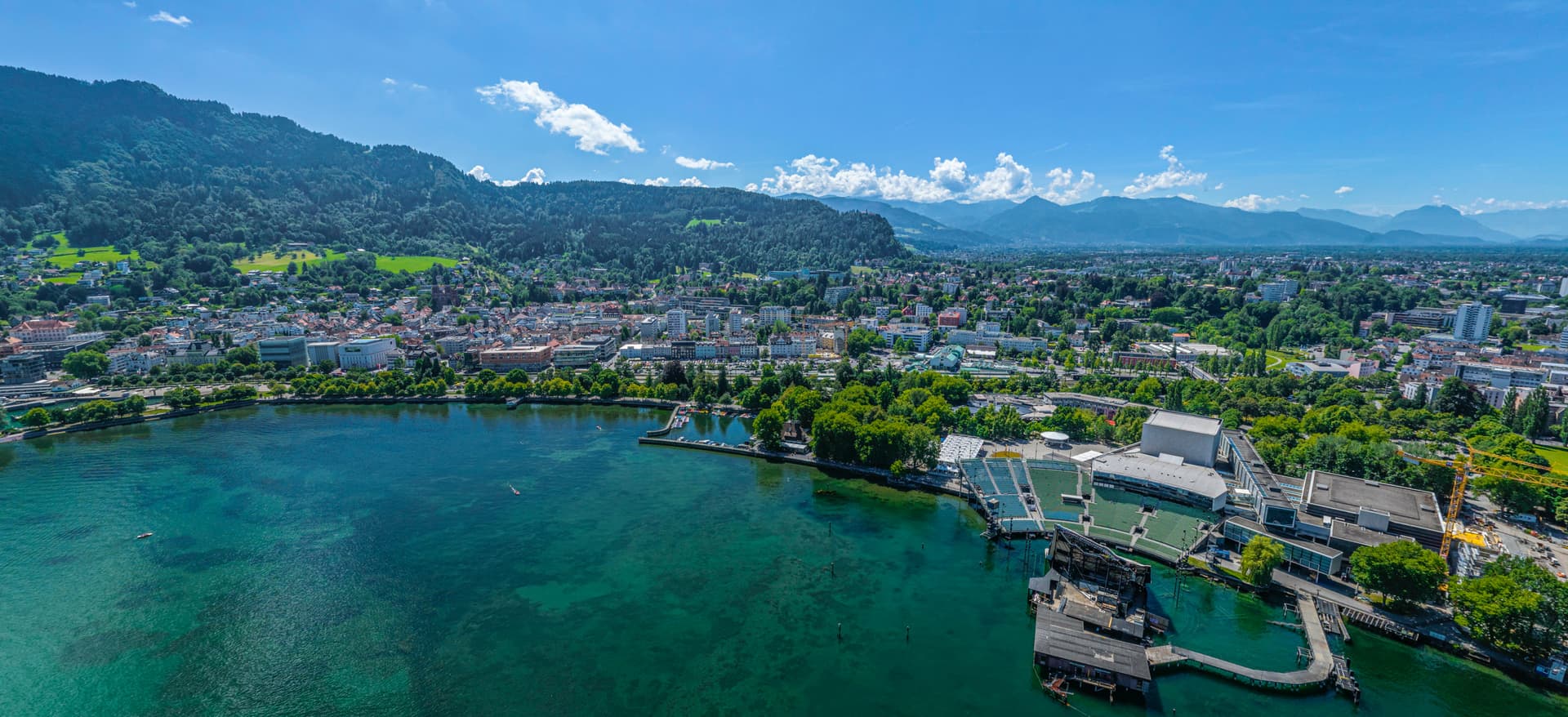 Aerial summer view of Bregenz am Bodensee city, green mountains, and floating stage on Lake Constance.