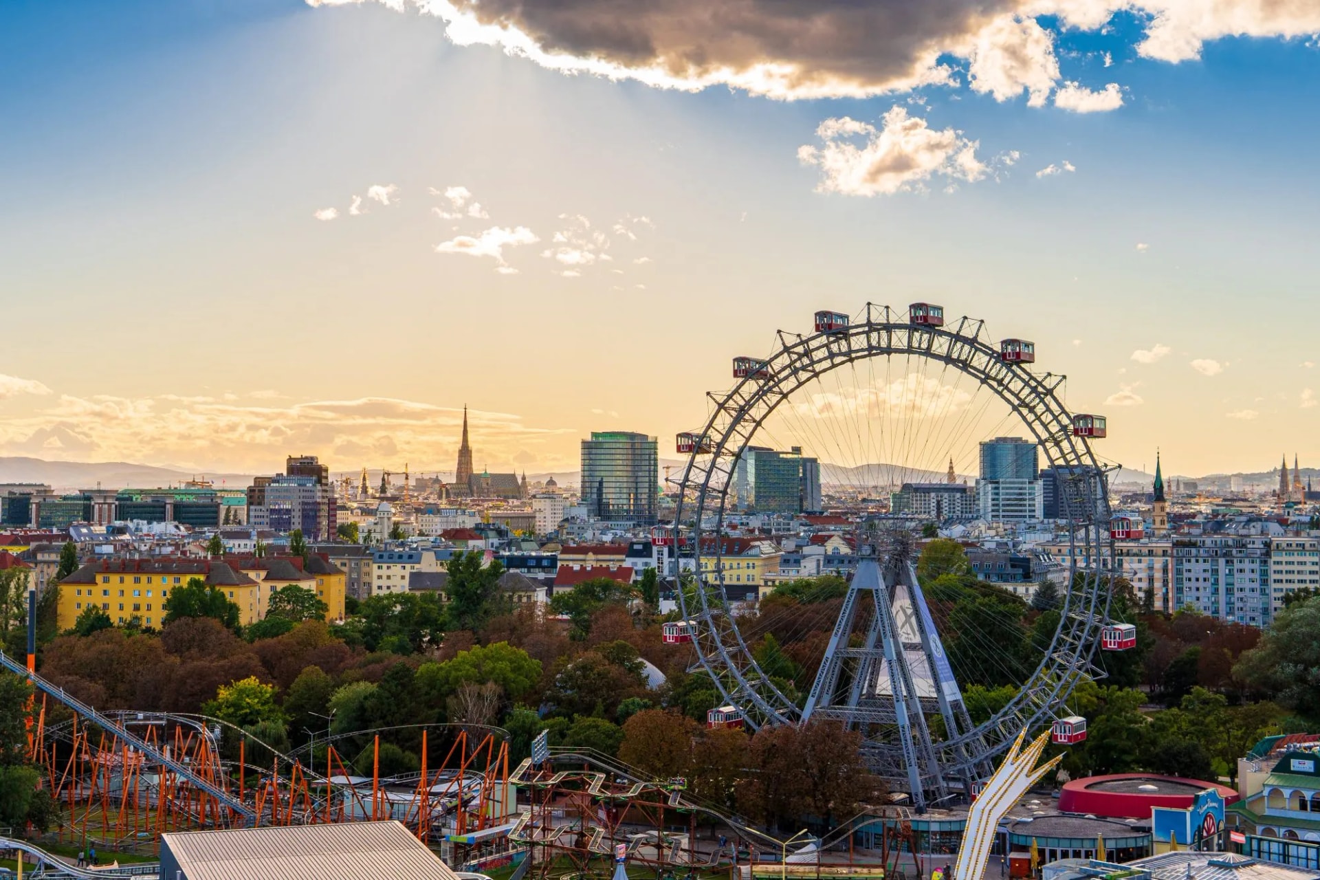 City view of Vienna, Austria, from above at Prater amusement park. Iconic fairy wheel and other amusement rides in the background with the sun peeking out of the clouds.