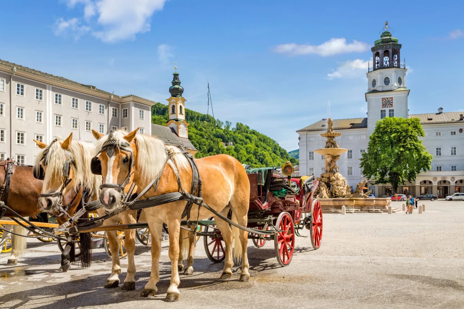 Horse-drawn carriage with two horses in Salzburg square with fountain and clock tower.