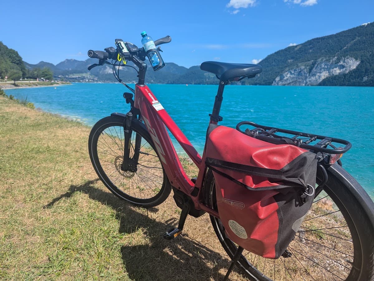 Red touring bicycle parked by a turquoise alpine lake with mountains in the background
