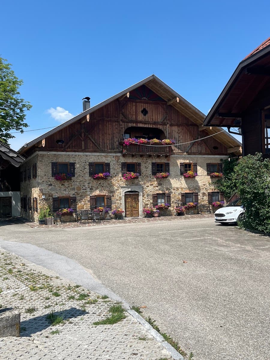 Traditional alpine house with stone walls, wooden upper floor, window boxes with flowers, and paved courtyard under clear ...