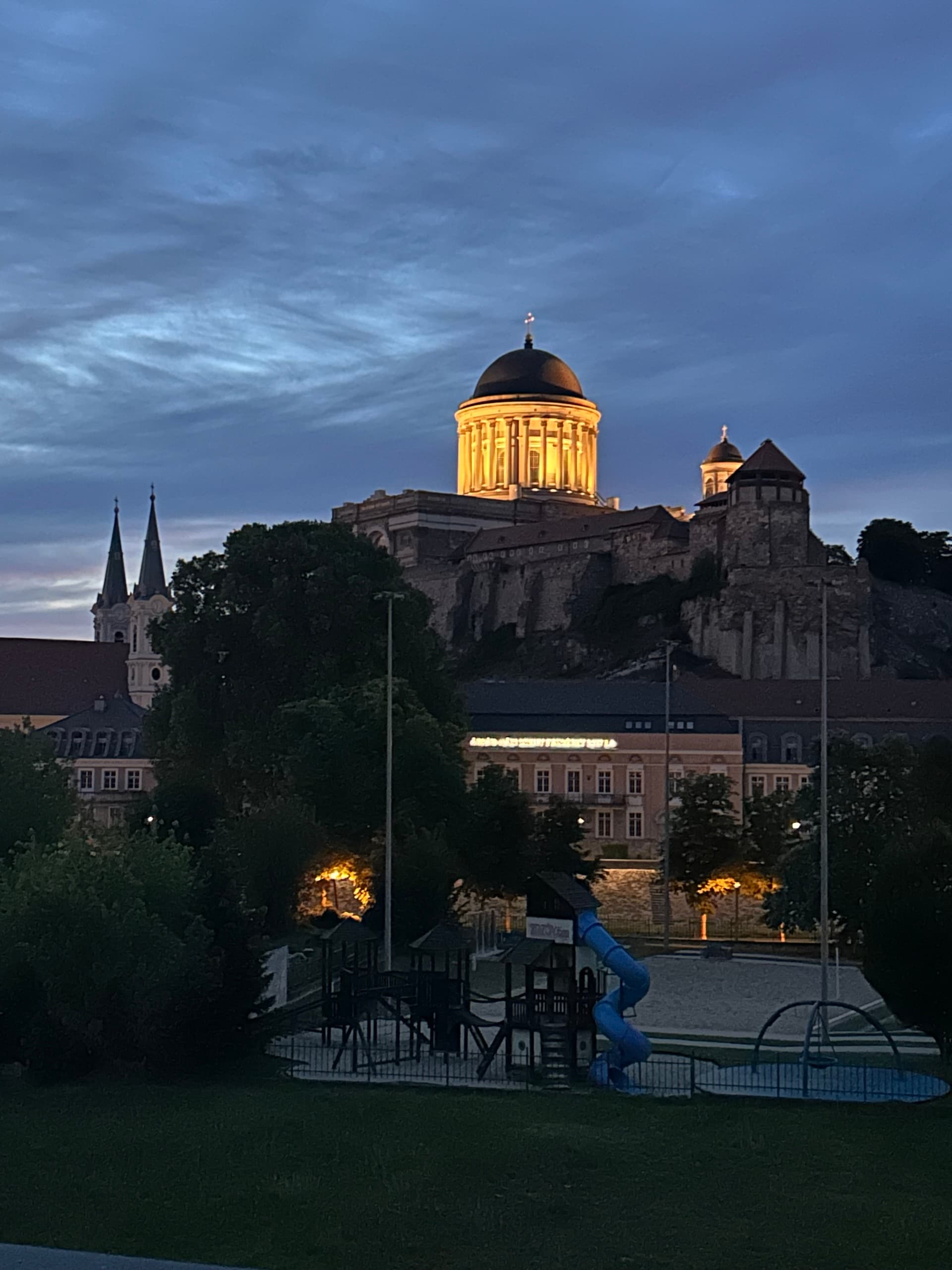 Esztergom Basilica illuminated at dusk above town buildings and a playground